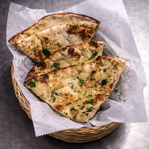 Three pieces of garlic naan bread with cilantro in a woven basket lined with white paper.