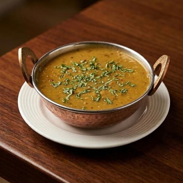 A copper bowl of Indian dal, garnished with fresh cilantro, sits on a white plate.