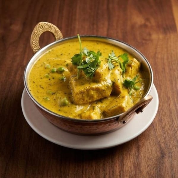 Mutter Paneer, a creamy yellow curry with paneer and peas, garnished with cilantro in a copper bowl.